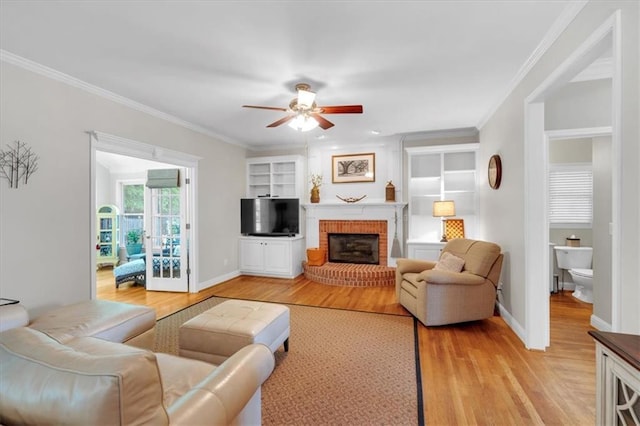 living room featuring crown molding, ceiling fan, a brick fireplace, and light wood-type flooring