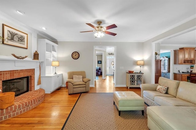 living room with ornamental molding, a fireplace, baseboards, light wood-type flooring, and a ceiling fan