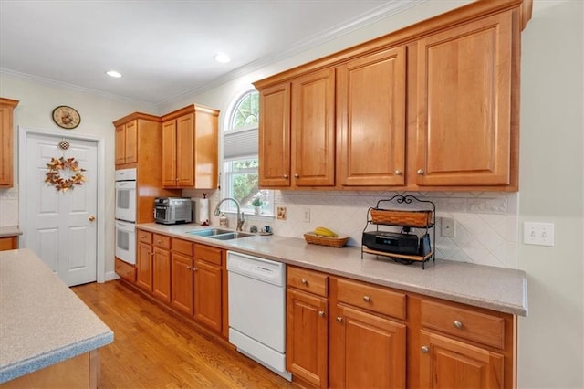 kitchen with white appliances, ornamental molding, a sink, and light countertops