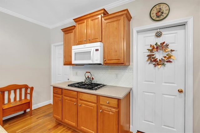 kitchen with decorative backsplash, ornamental molding, white microwave, gas stovetop, and light wood-style flooring