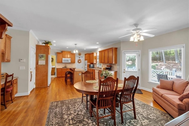 dining space with baseboards, ornamental molding, a ceiling fan, and light wood-style flooring