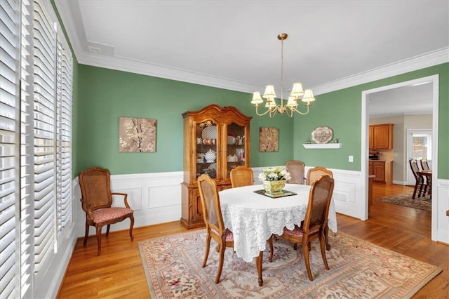 dining area with an inviting chandelier, ornamental molding, wainscoting, a decorative wall, and light wood-style flooring