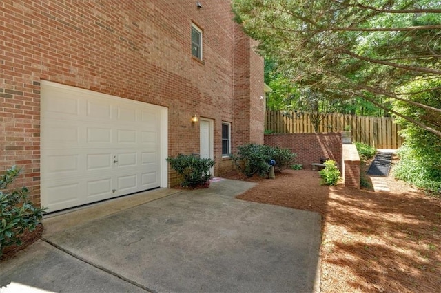 view of home's exterior featuring concrete driveway, brick siding, fence, and a garage