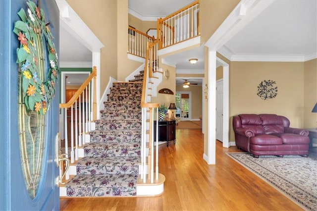 foyer entrance with ornamental molding, a ceiling fan, wood finished floors, and stairway