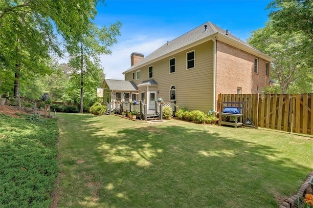 back of house with a yard, a deck, fence, and a chimney