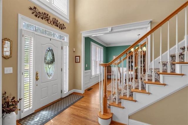 foyer entrance with stairway, a wainscoted wall, ornamental molding, and light wood-style flooring