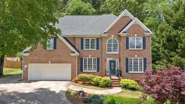 colonial home with fence, an attached garage, driveway, and brick siding