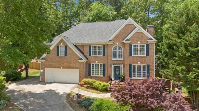 colonial-style house with driveway, a chimney, a garage, brick siding, and fence