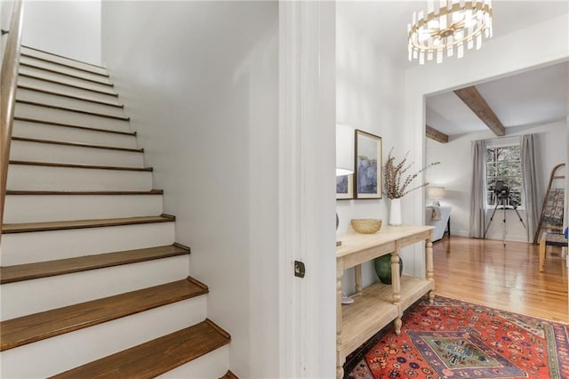 stairway featuring hardwood / wood-style floors, beamed ceiling, and an inviting chandelier