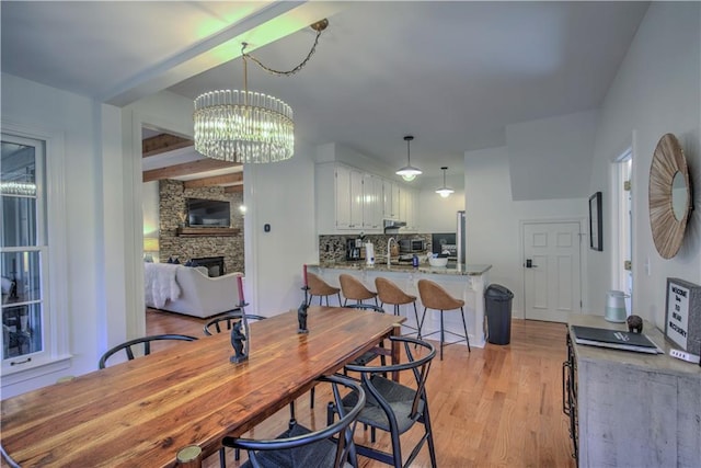 dining room with beam ceiling, sink, a chandelier, light hardwood / wood-style floors, and a fireplace