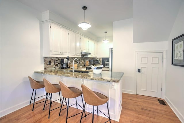 208 Trout Lily Trl, Big Canoe, GA 30143 - kitchen featuring under cabinet range hood, a peninsula, decorative backsplash, light stone counters, and light wood-type flooring