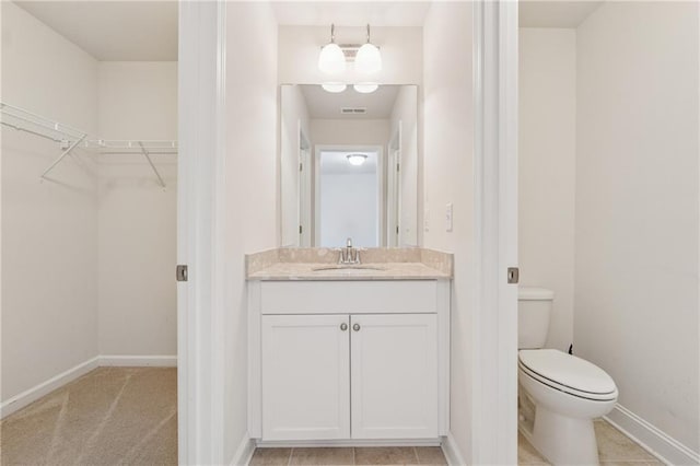 bathroom with a spacious closet, toilet, vanity, and baseboards