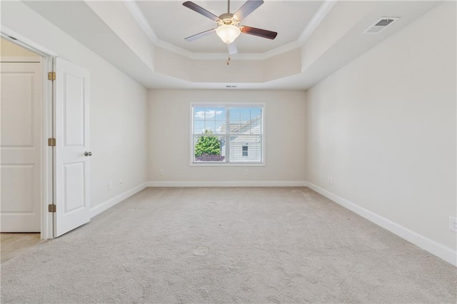 empty room featuring a tray ceiling, ceiling fan, ornamental molding, light carpet, and baseboards