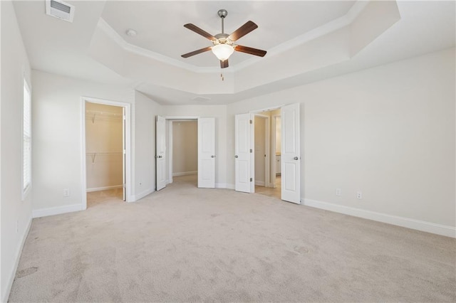unfurnished bedroom with a raised ceiling, light colored carpet, a walk in closet, and baseboards