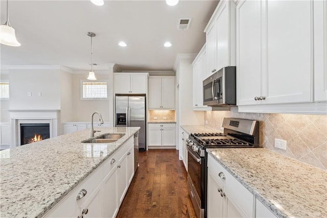 kitchen featuring appliances with stainless steel finishes, a sink, a warm lit fireplace, white cabinetry, and ornamental molding