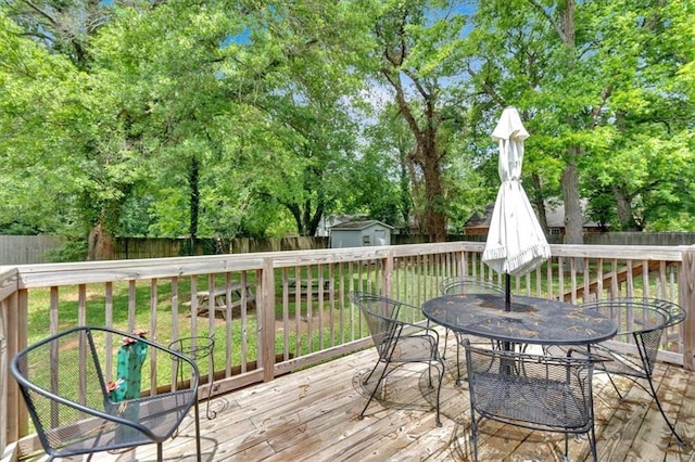 deck featuring outdoor dining space, a storage unit, an outdoor structure, and view of wooded area