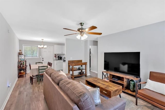 living area with a chandelier, light wood finished floors, a ceiling fan, and baseboards