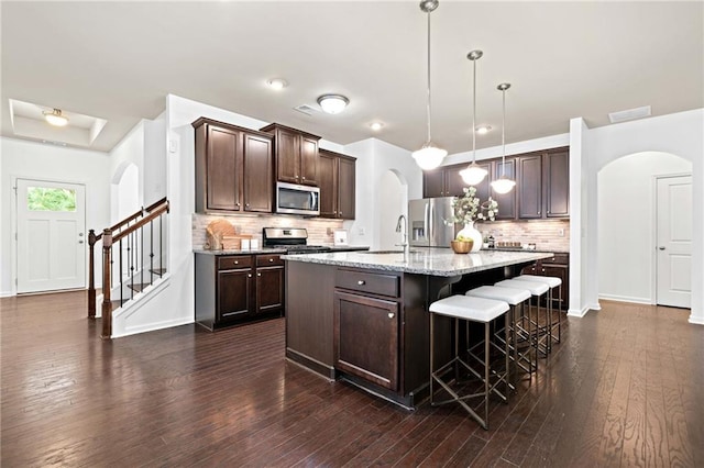 123 Meridian Dr, Woodstock, GA 30188 - kitchen featuring arched walkways, appliances with stainless steel finishes, dark brown cabinetry, a kitchen bar, and backsplash