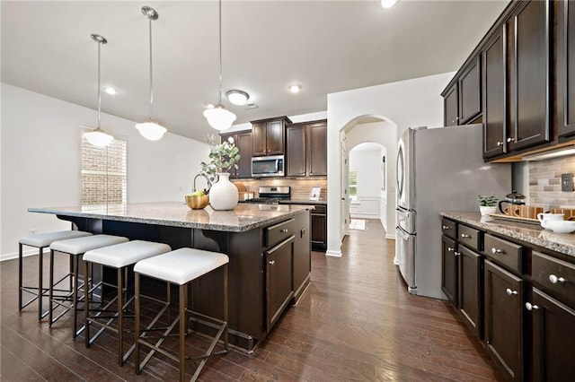 123 Meridian Dr, Woodstock, GA 30188 - kitchen featuring stainless steel appliances, arched walkways, a kitchen island with sink, dark wood-style floors, and dark brown cabinets