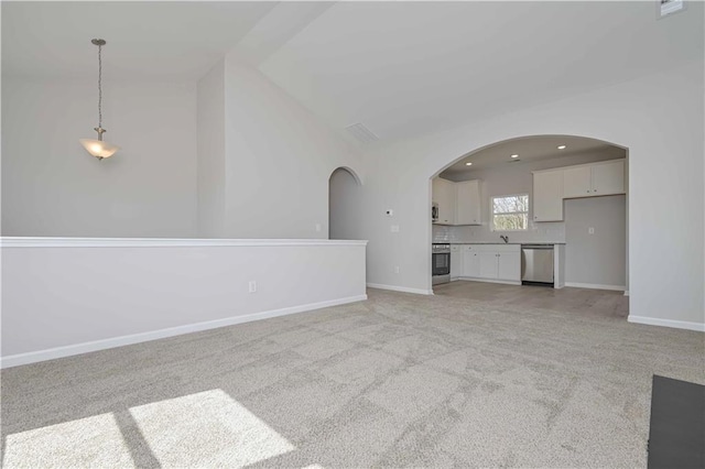 unfurnished living room featuring light carpet, baseboards, vaulted ceiling, and arched walkways