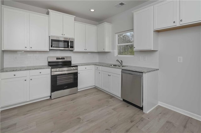 kitchen with light wood-style flooring, light stone counters, stainless steel appliances, white cabinetry, and visible vents