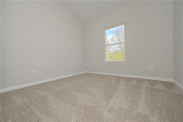 empty room with light colored carpet, vaulted ceiling, and baseboards
