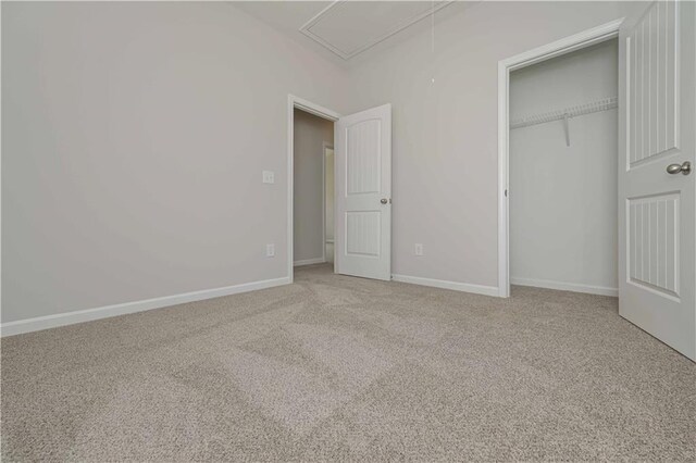unfurnished bedroom with baseboards, attic access, light carpet, and a closet