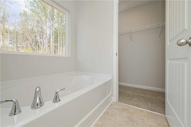 full bathroom with a garden tub, baseboards, and a spacious closet