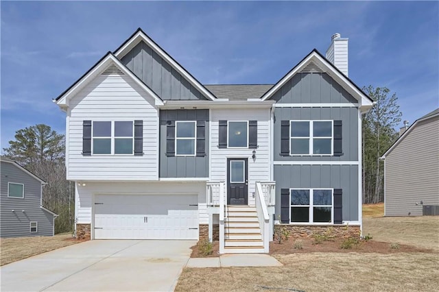 bi-level home featuring driveway, board and batten siding, stone siding, a chimney, and an attached garage