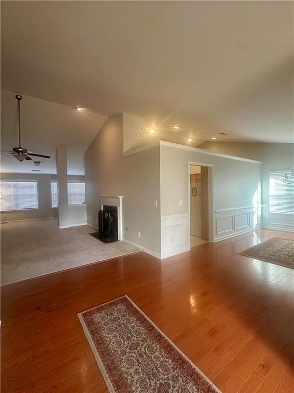 unfurnished living room featuring wood finished floors, lofted ceiling, ceiling fan, a decorative wall, and wainscoting