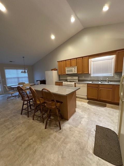 kitchen featuring white appliances, a kitchen bar, a kitchen island, a sink, and brown cabinetry