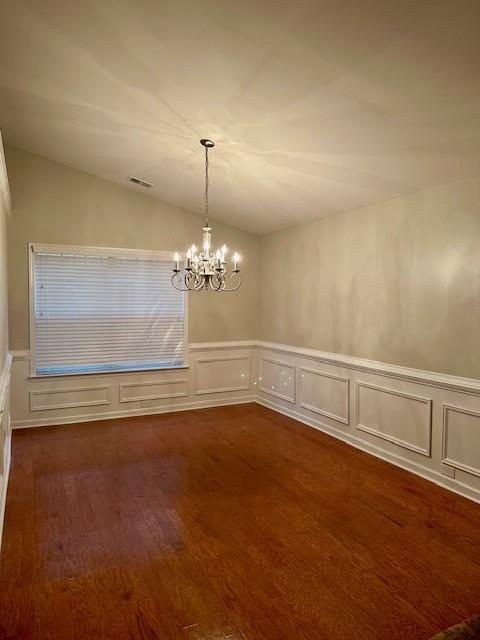 unfurnished dining area featuring dark wood-style flooring, visible vents, an inviting chandelier, vaulted ceiling, and wainscoting