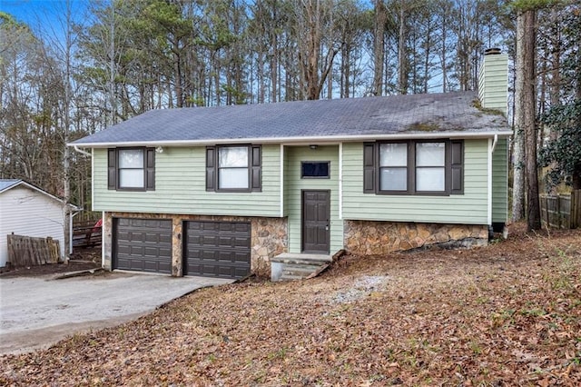 split foyer home featuring driveway, a chimney, an attached garage, and a shingled roof