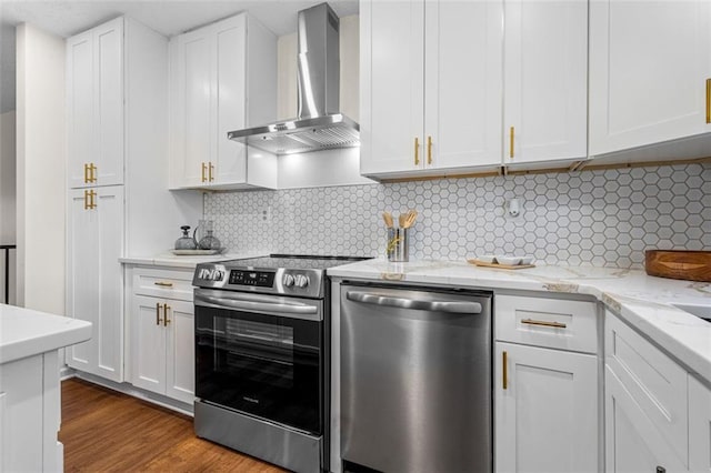 kitchen with tasteful backsplash, appliances with stainless steel finishes, wood finished floors, white cabinets, and wall chimney exhaust hood