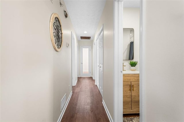 corridor with visible vents, baseboards, a textured ceiling, and dark wood-style floors