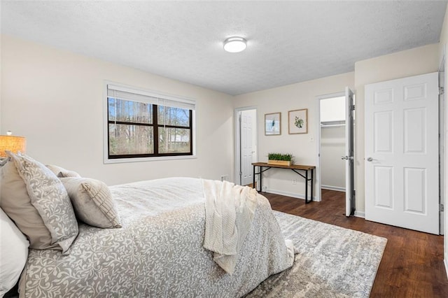 bedroom with a walk in closet, a textured ceiling, dark wood finished floors, a closet, and baseboards