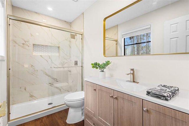 bathroom with vanity, toilet, wood finished floors, and a marble finish shower