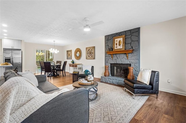 living area with ceiling fan with notable chandelier, a stone fireplace, wood finished floors, and baseboards