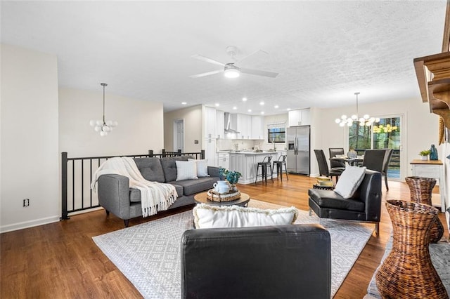 living room featuring ceiling fan with notable chandelier, a textured ceiling, and wood finished floors