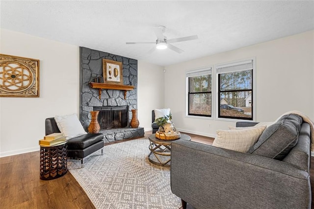 living room with baseboards, a stone fireplace, wood finished floors, and a ceiling fan