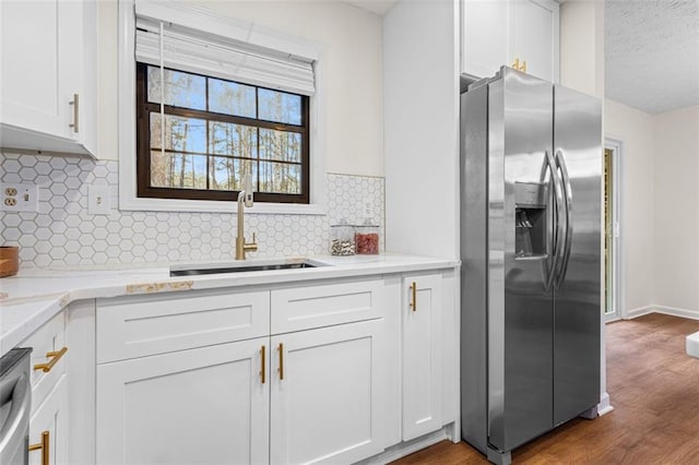 kitchen with stainless steel refrigerator with ice dispenser, a sink, backsplash, dark wood-style floors, and white cabinetry