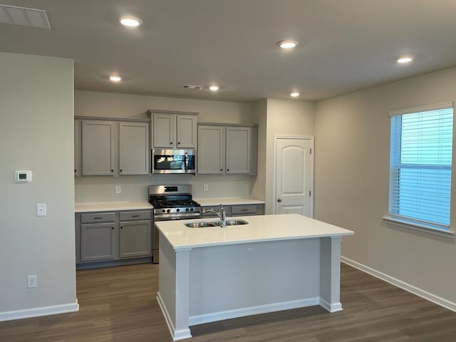 kitchen with stainless steel appliances, a center island with sink, dark wood-type flooring, and gray cabinetry