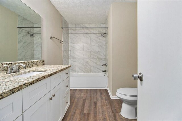 full bathroom with hardwood / wood-style floors, a textured ceiling, toilet, vanity, and tiled shower / bath