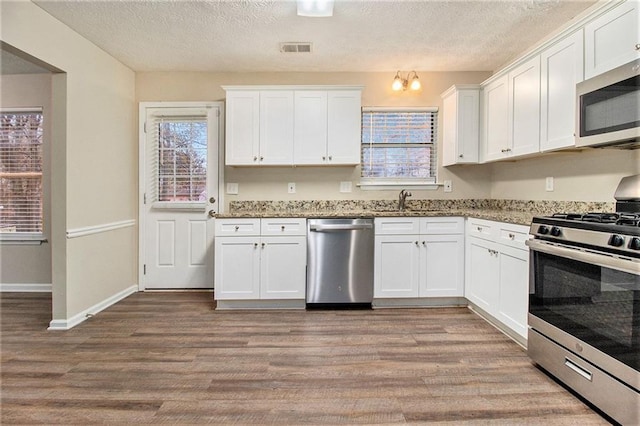 kitchen with white cabinets, stainless steel appliances, light hardwood / wood-style flooring, and light stone counters