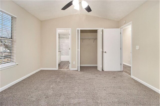 unfurnished bedroom with vaulted ceiling, carpet flooring, ceiling fan, ensuite bath, and a closet