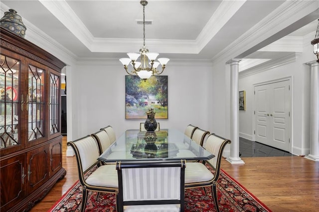 dining space featuring a tray ceiling, an inviting chandelier, wood finished floors, and ornate columns