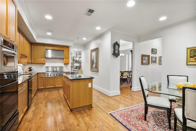 kitchen with light wood finished floors, visible vents, a kitchen island with sink, crown molding, and under cabinet range hood