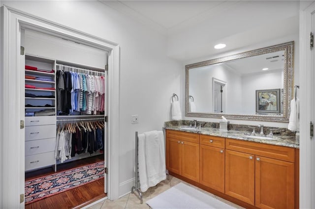 full bath with double vanity, ornamental molding, a sink, and a walk in closet