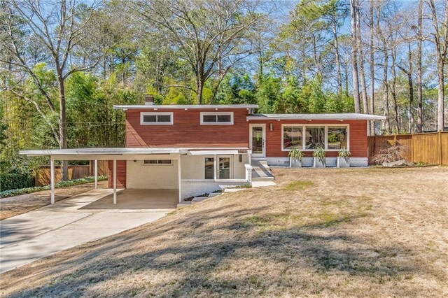 rear view of property with fence, a garage, driveway, and a lawn