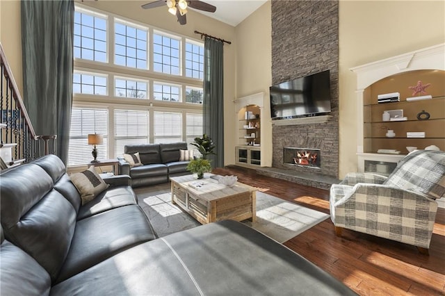 living room with hardwood / wood-style flooring, ceiling fan, a high ceiling, a fireplace, and built in shelves